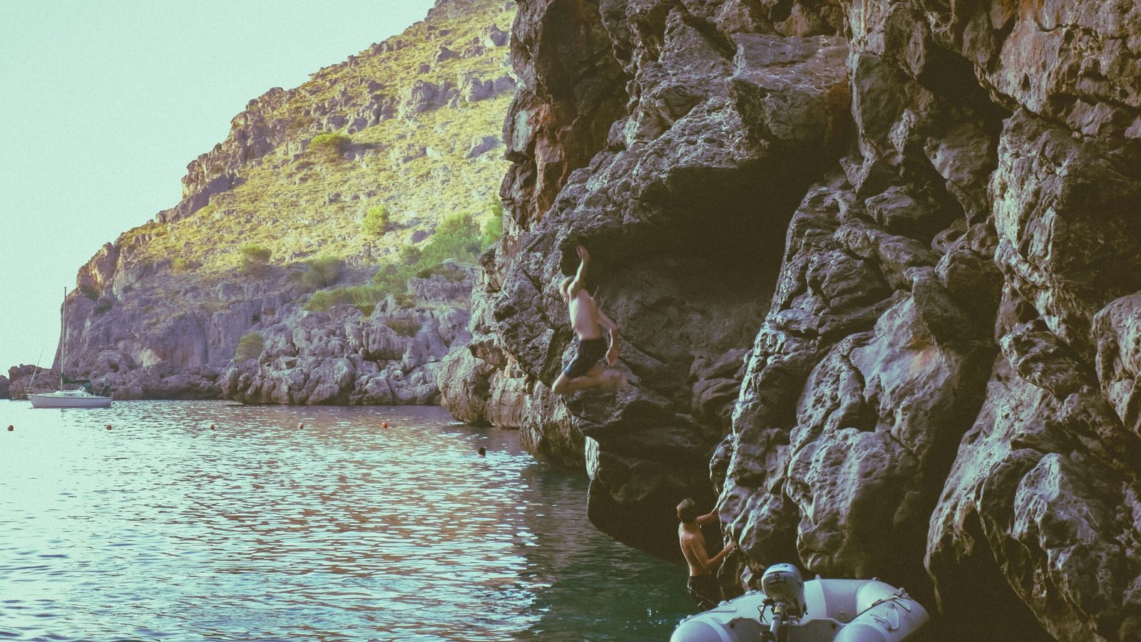 A group of people standing on the side of a cliff next to a body of